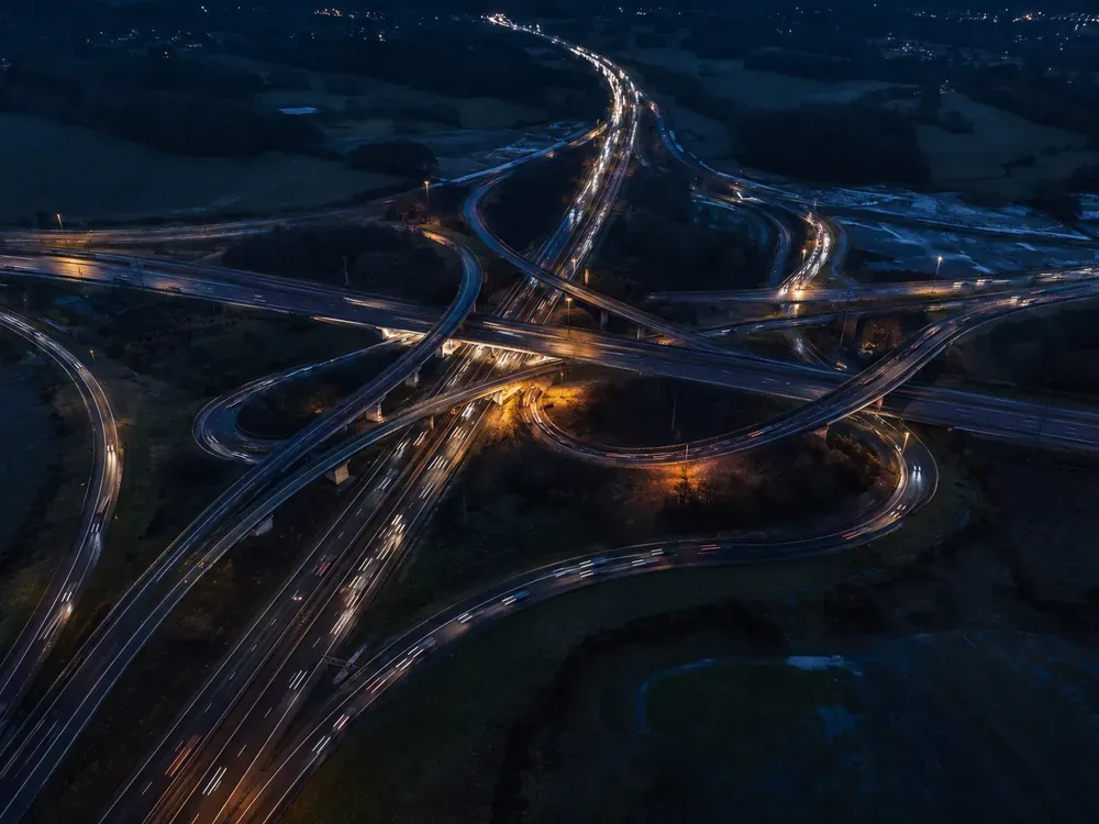 Vue aérienne d'un échangeur autoroutier à la tombée de la nuit, boucles de bretelles et traînées de phares